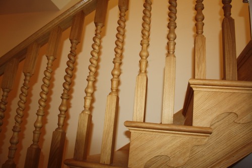 Wooden staircase with intricately carved, twisted balusters and a smooth handrail, creating a warm and classic look. The steps are visible, showing the craftsmanship in the design. Warm lighting adds to the cozy atmosphere.