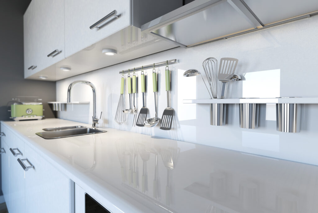 A modern, sleek white kitchen with a shiny countertop, stainless steel sink, green-accented utensils hanging on a rack, shelves holding metal containers, and a green toaster in the background.